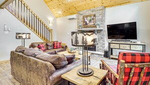 A modern living room with a wooden ceiling, a stone fireplace, a large flat-screen TV, and a staircase. - Forest Views & Hot Tub: Poconos Cozy Cabin (Albrightsville)
