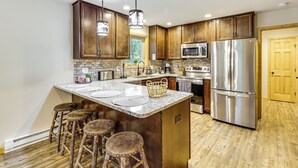 A modern kitchen with wooden cabinets, stainless steel appliances, and a central island with stools. - Forest Views & Hot Tub: Poconos Cozy Cabin (Albrightsville)