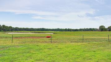 A large, open grassy field with a dirt track and a red object in the distance.
