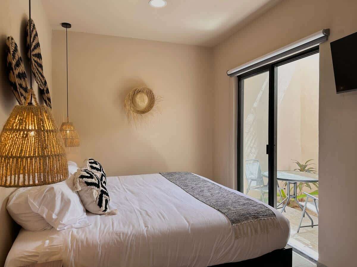 A bedroom with a bed, a hanging light fixture, a wall decoration, and a view of the outside.