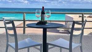 Une table avec deux verres à vin et une bouteille, donnant sur une mer turquoise.