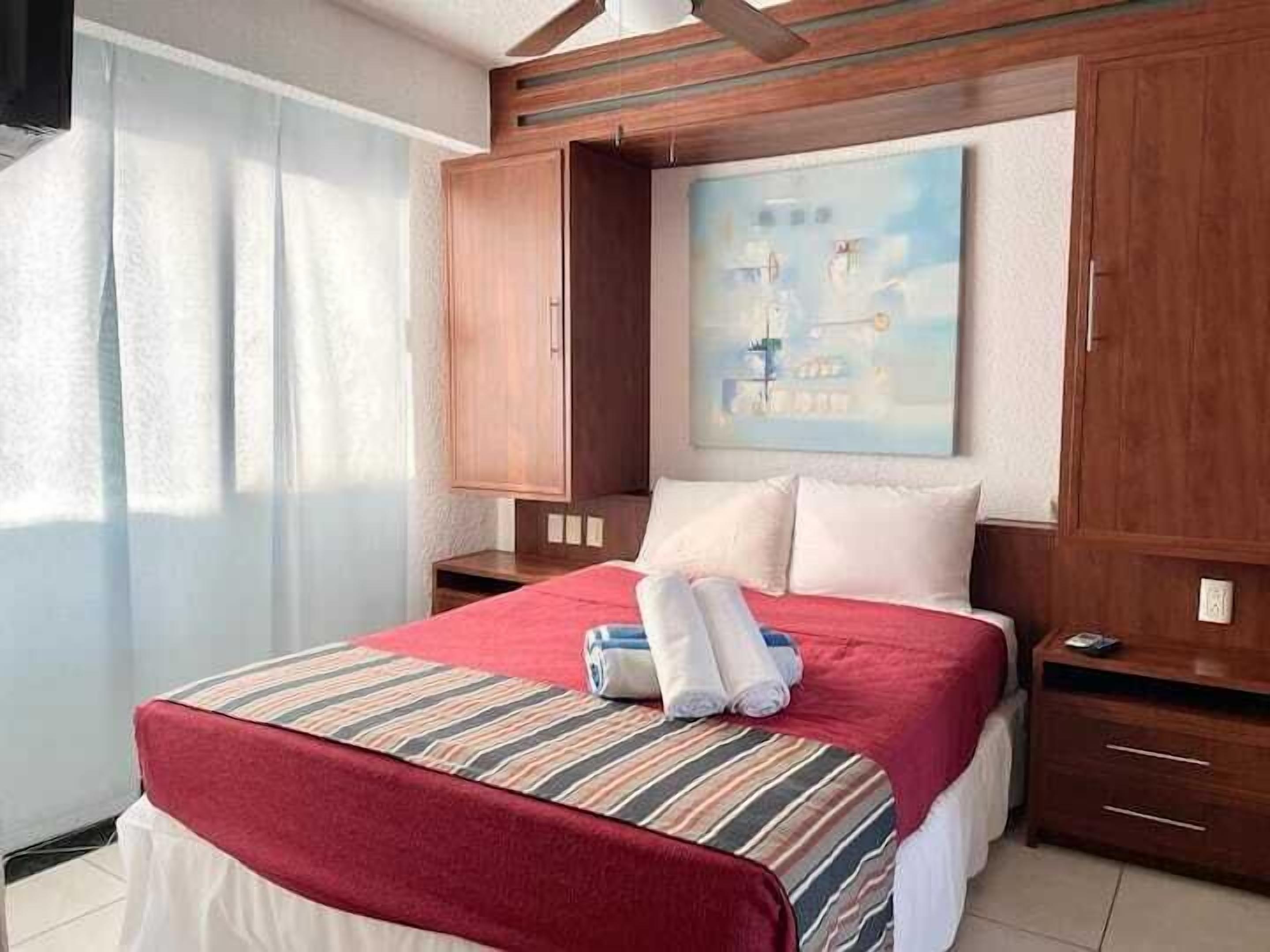 A hotel room with a bed, a painting, a wooden wardrobe, and a window with curtains.