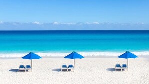 Une plage avec trois parasols bleus et des chaises longues blanches.