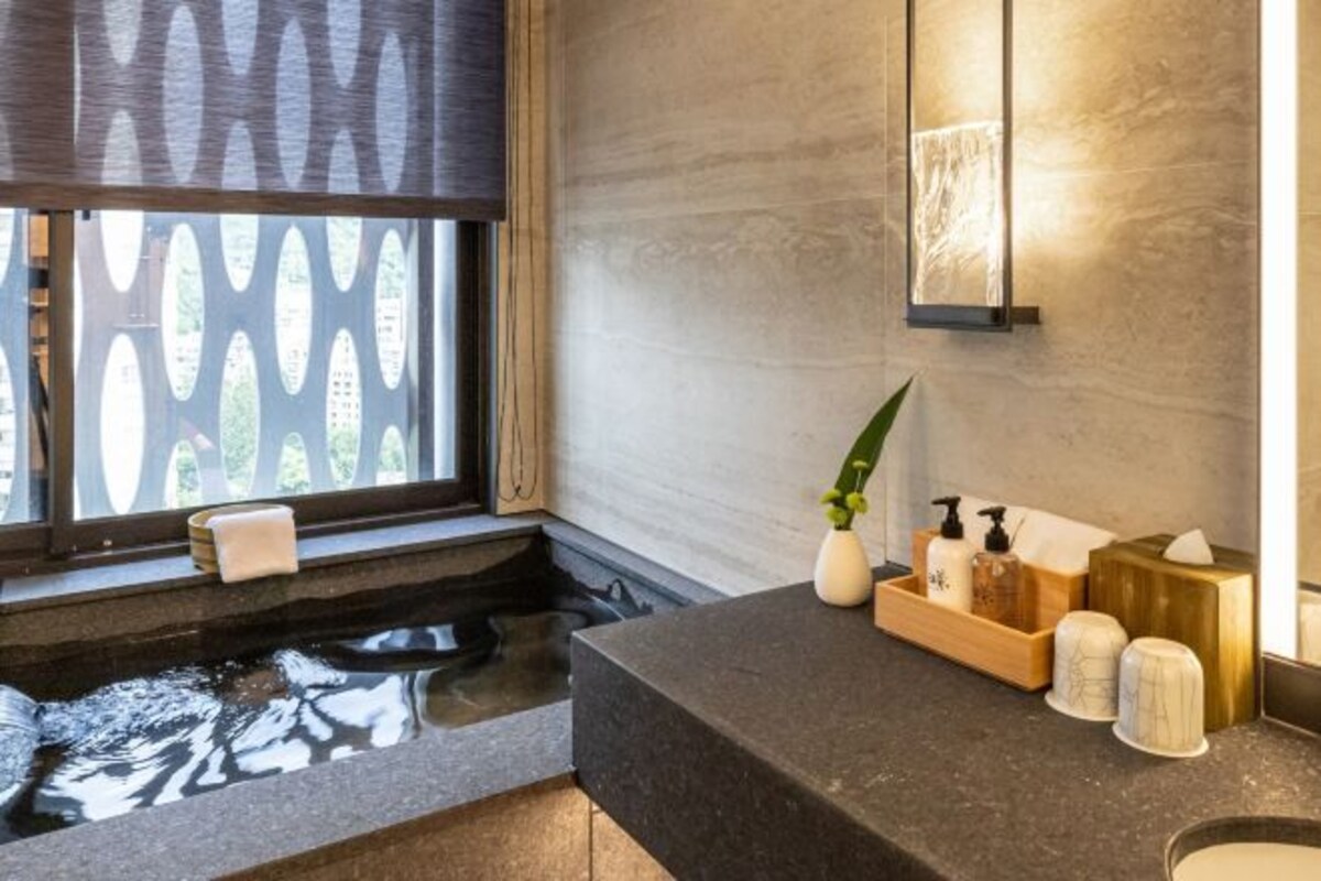 A modern bathroom with a large window, a bathtub, and a vanity with toiletries.