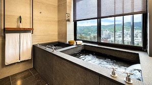 A modern bathroom with a large soaking tub, a window with a city view, and a shelf with a plant. - Wellspring by Silks Beitou (Taipei)