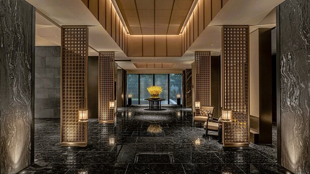 A modern lobby with a marble floor, tall wooden screens, and a central table with flowers. - Wellspring by Silks Beitou (Taipei)