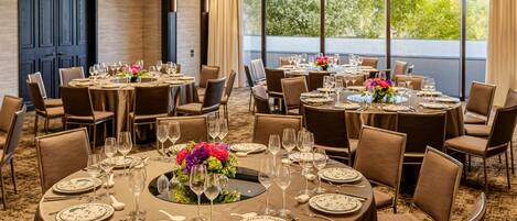 A hotel dining area with round tables set for six, each with floral centerpieces, wine glasses, and cutlery.