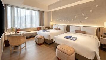 Quarto de hotel moderno com duas camas, um sofá, uma mesa de jantar e vista para a cidade.
