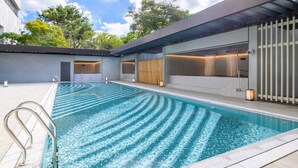A modern outdoor swimming pool with clear blue water, surrounded by a covered area with seating and a wooden door. - Wellspring by Silks Beitou (Taipei)