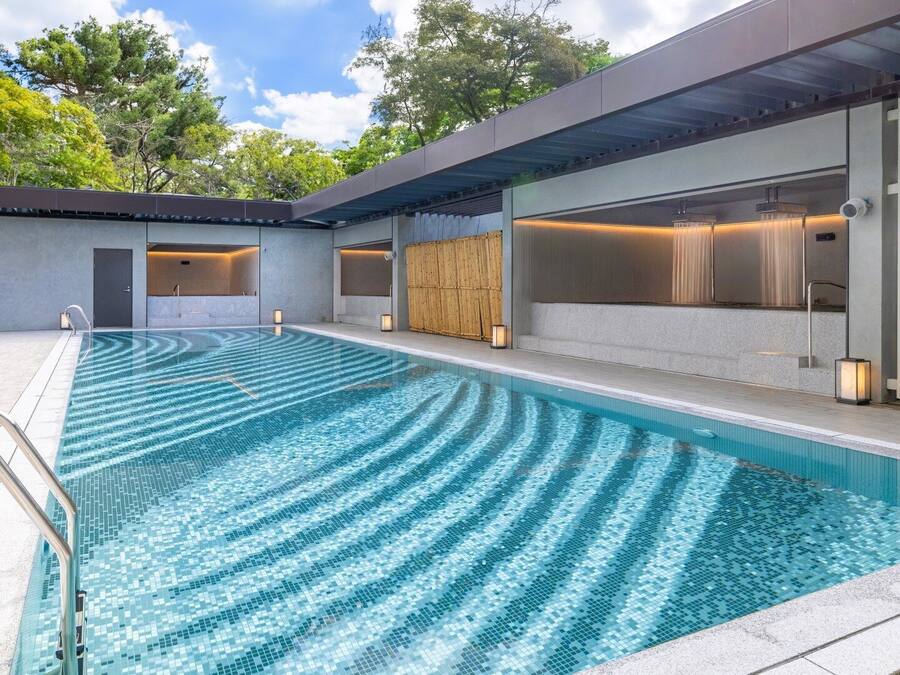 Una piscina exterior moderna con agua azul cristalina, rodeada por una zona cubierta con asientos y una puerta de madera.