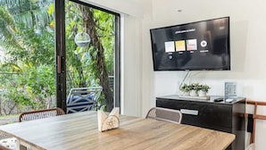 A dining area with a wooden table, chairs, a television mounted on the wall, and a view of greenery outside. - Studio in Cancun Hotel Zone | Steps to Beach (Cancún)