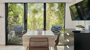 A modern kitchen with a large window, a dining table, chairs, a TV, and a black cabinet. - Studio in Cancun Hotel Zone | Steps to Beach (Cancún)
