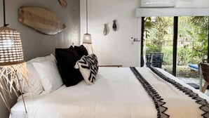 A bedroom with a bed, pillows, a hanging light fixture, a wall-mounted air conditioner, and a view of greenery outside. - Studio in Cancun Hotel Zone | Steps to Beach (Cancún)