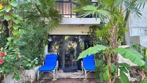 A two-story building with a balcony, surrounded by lush greenery and two blue chairs in front of the entrance. - Studio in Cancun Hotel Zone | Steps to Beach (Cancún)