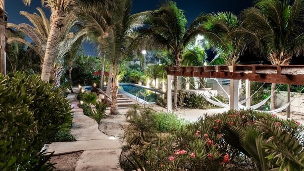 Un sendero nocturno en un resort con palmeras, una piscina y una hamaca.