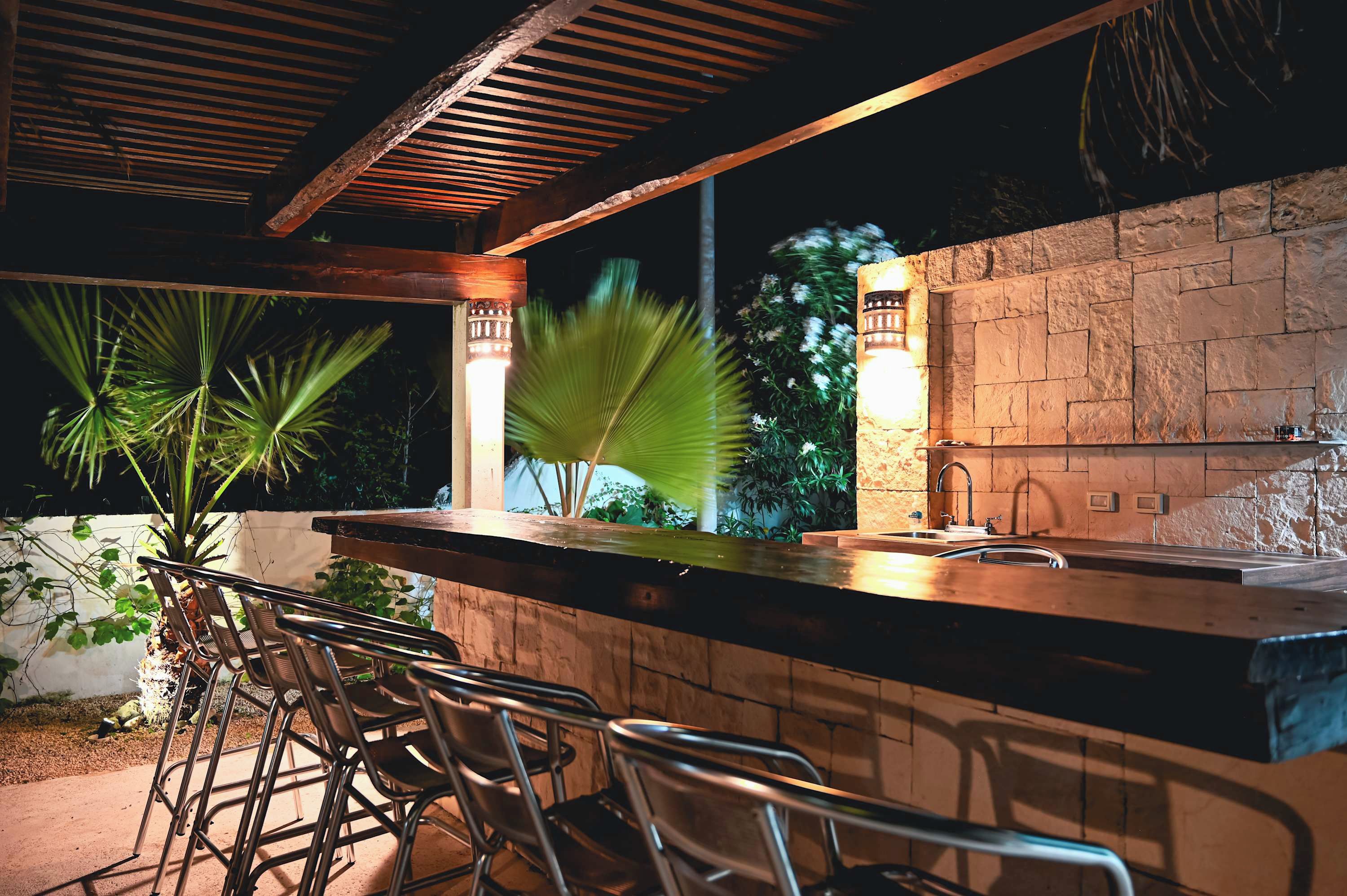 An outdoor bar area with a stone wall, a sink, and chairs.