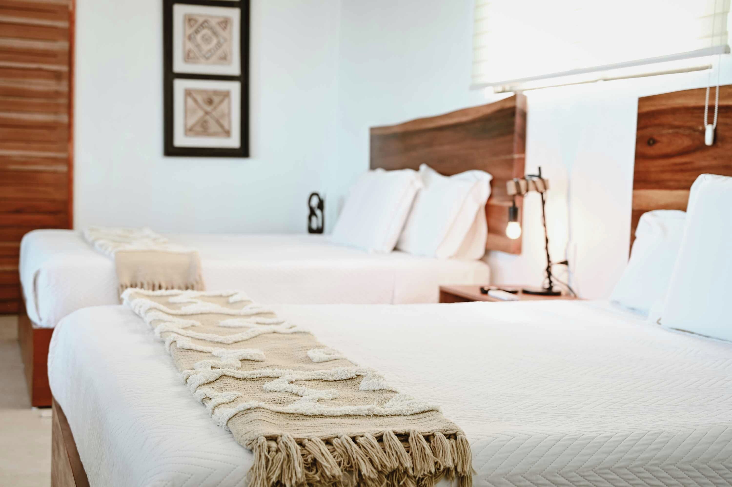Une chambre d’hôtel avec deux lits, une tête de lit en bois, une table de chevet avec une lampe et un mur orné de tableaux encadrés.