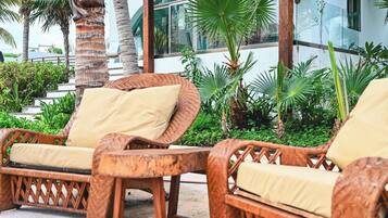 Sillones de mimbre con cojines en un entorno exterior con palmeras y un edificio moderno al fondo.