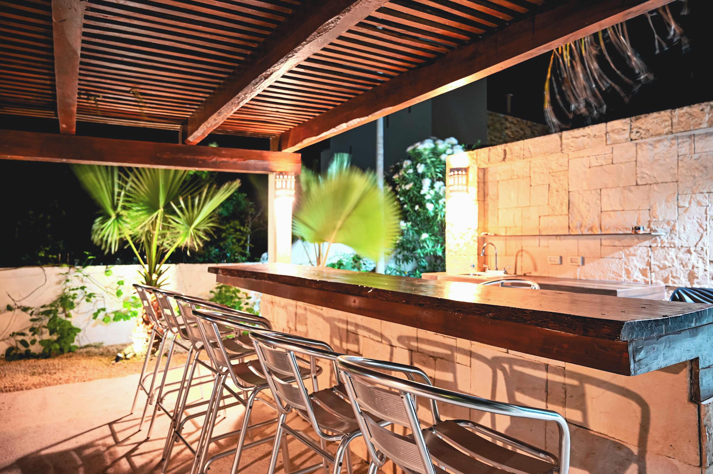 An outdoor bar area with metal chairs, a wooden counter, and a stone wall.