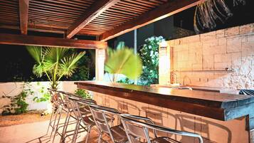 An outdoor bar area with metal chairs, a wooden counter, and a stone wall.