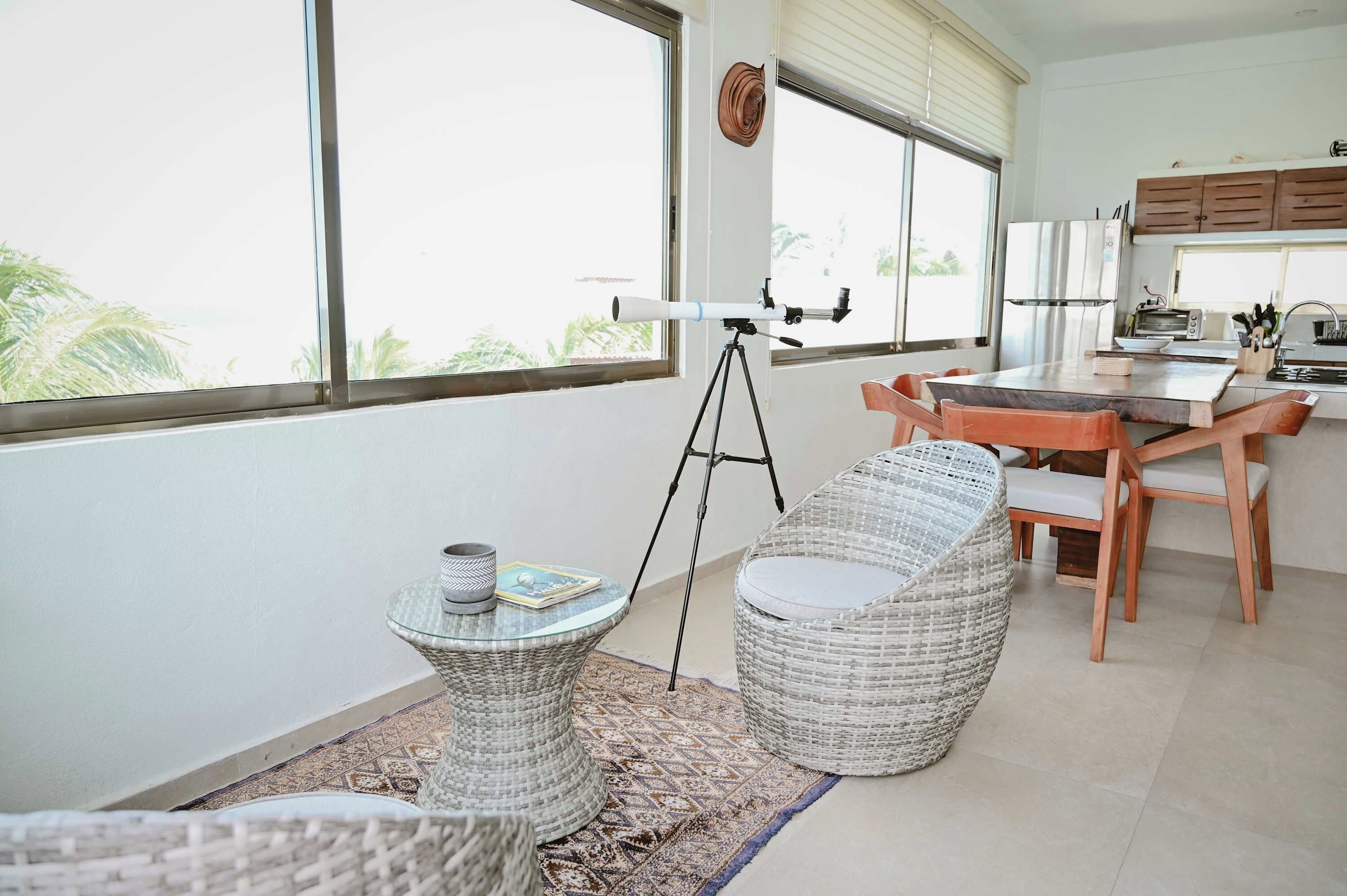 A modern kitchen with a dining area, a telescope, and a view of palm trees.