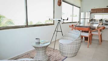 A modern kitchen with a dining area, a telescope, and a view of palm trees.