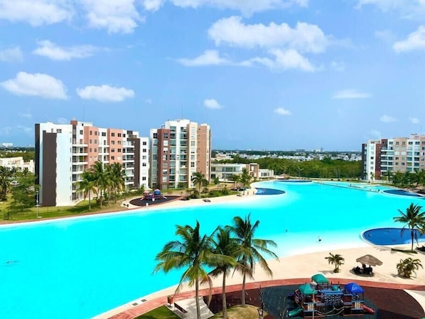 Relax by the resort's large pool surrounded by palm trees and a sandy beach area.