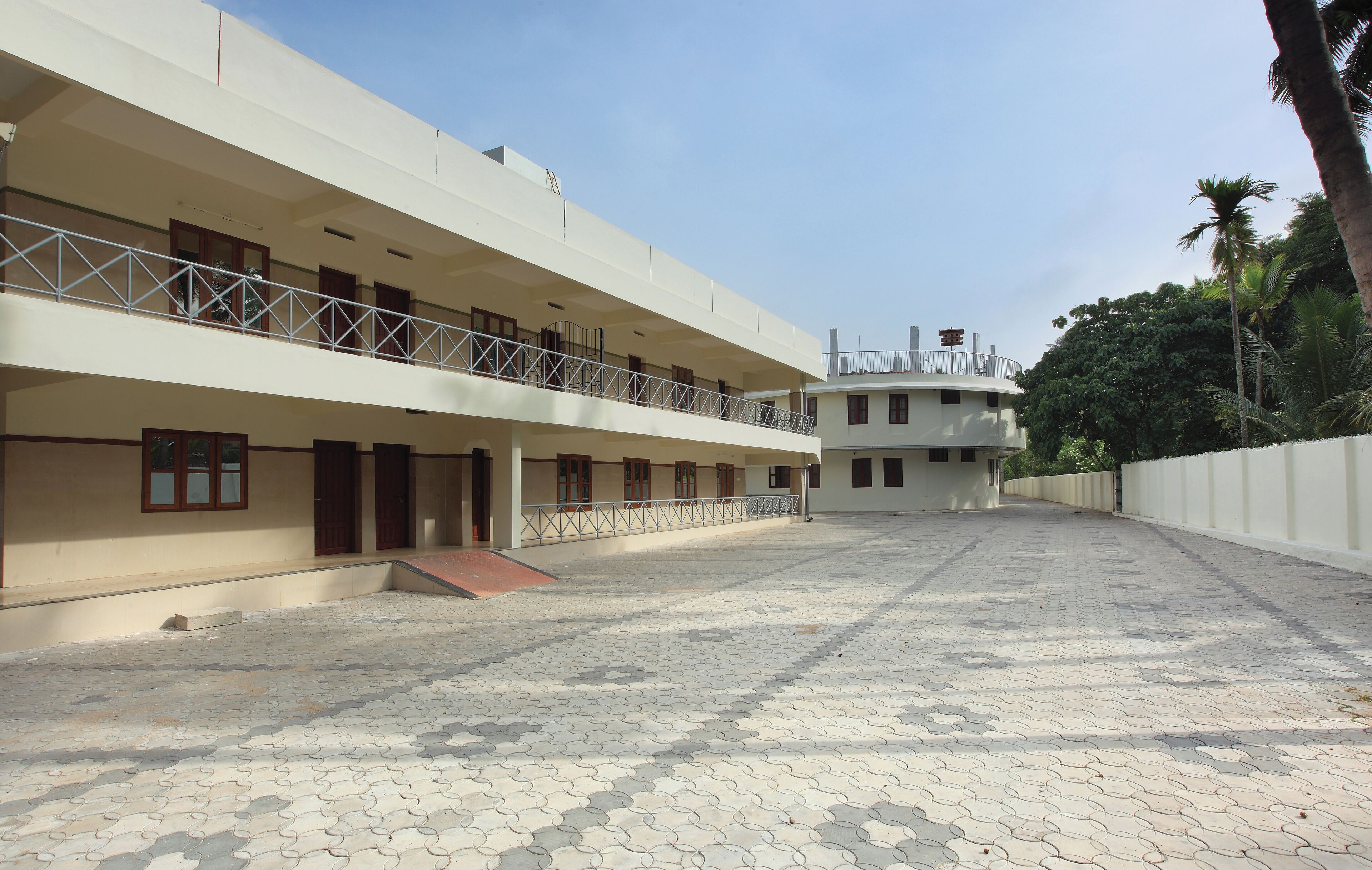 A multi-story building with a flat roof, a balcony on the ground floor, and a paved courtyard.