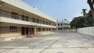 A multi-story building with a flat roof, a balcony on the ground floor, and a paved courtyard.