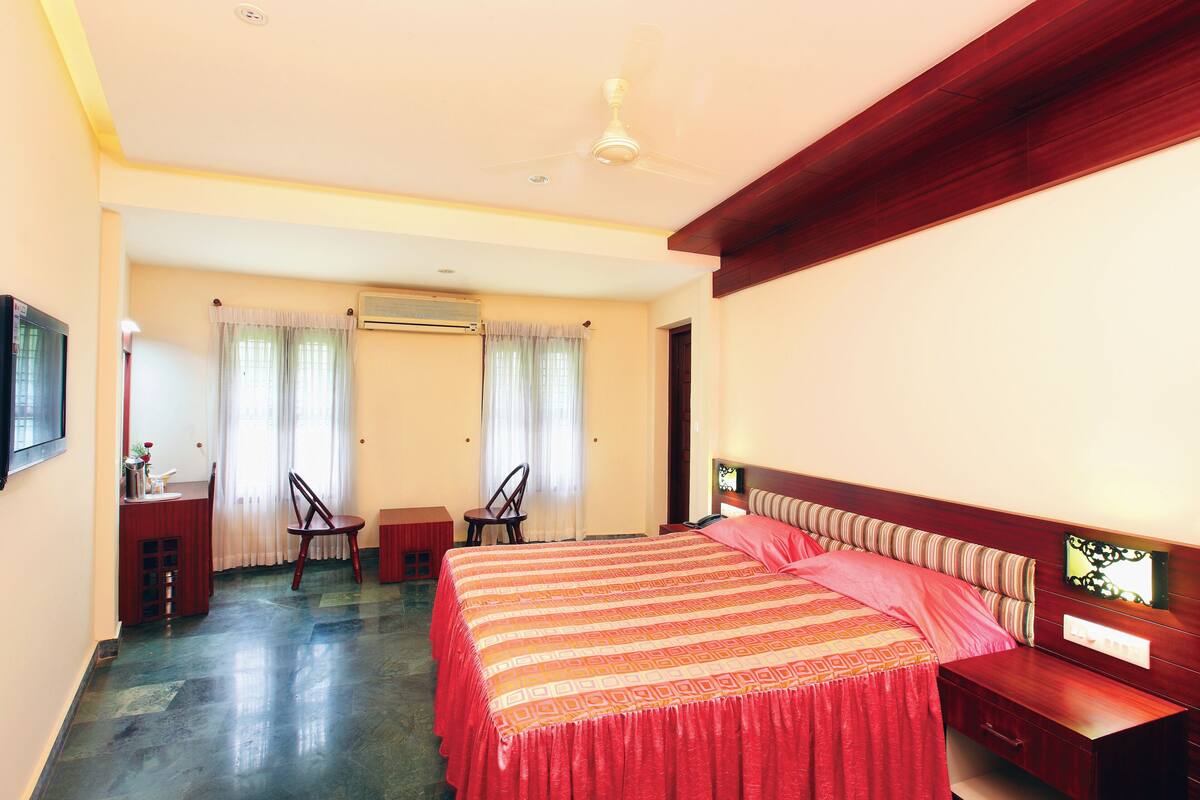 A hotel room with a large bed, a desk with a chair, a ceiling fan, and a window with curtains.