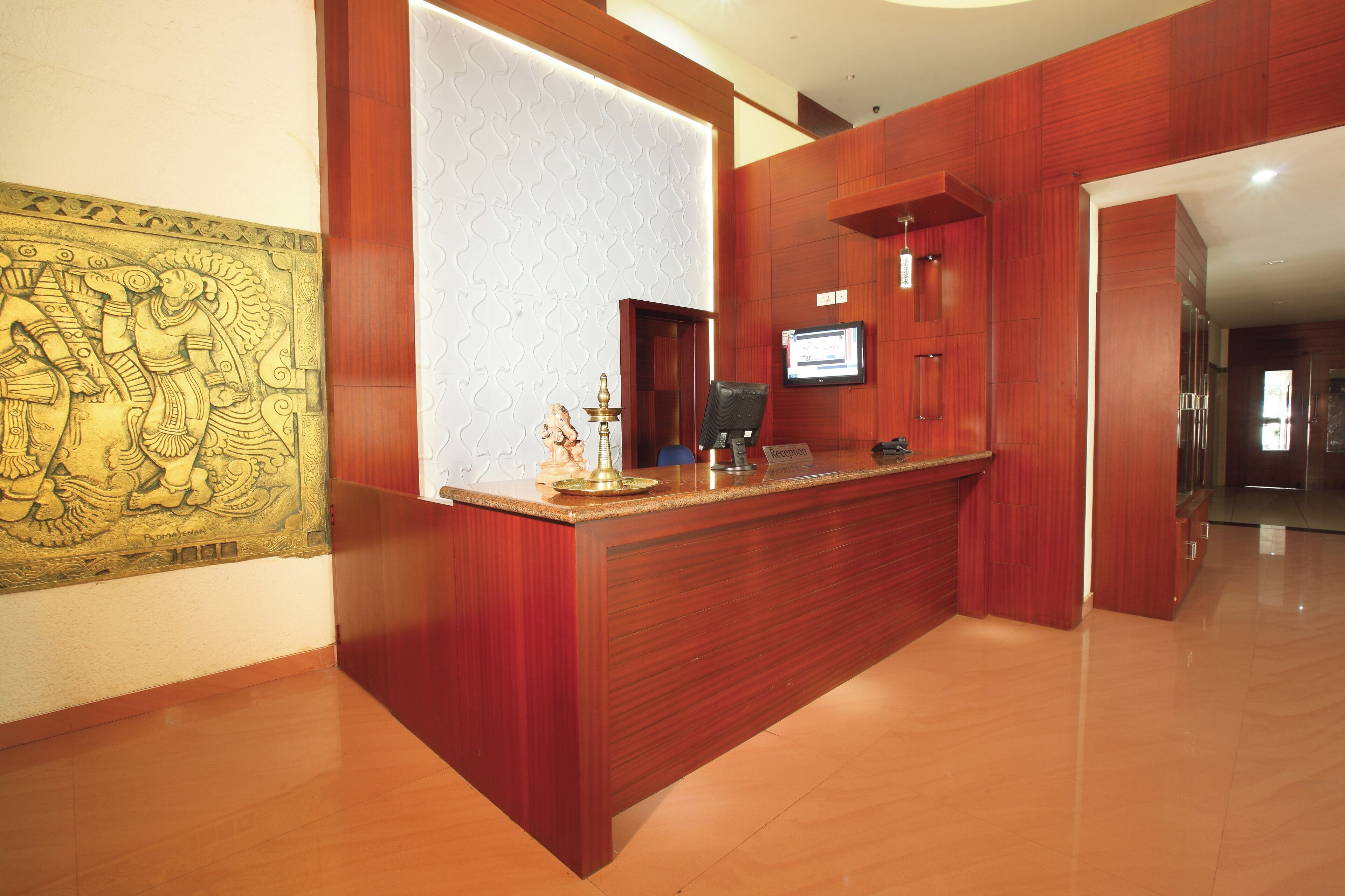A reception desk with a wooden finish, a wall-mounted television, and a decorative brass lamp.