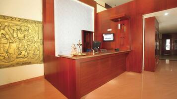 A reception desk with a wooden finish, a wall-mounted television, and a decorative brass lamp.