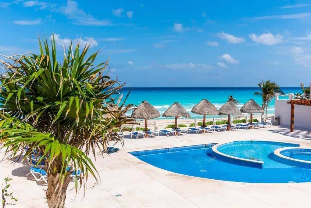 A pool area with lounge chairs and umbrellas, a beach view, and a clear sky.