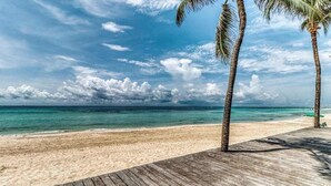 Une terrasse en bois qui mène à une plage bordée d’une eau turquoise cristalline et de palmiers.
