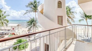 Un hôtel situé en bord de mer, doté d’un balcon, de palmiers et offrant une vue sur l’océan.