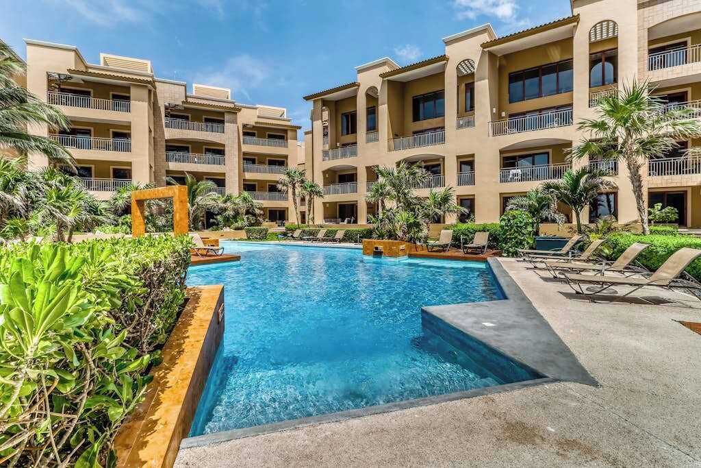 A hotel with a central swimming pool, multiple balconies, and lush greenery.