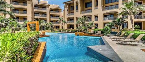 A hotel with a central swimming pool, multiple balconies, and lush greenery.