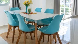 A dining area with a white table, blue chairs, a vase with yellow flowers, and a woven rug. - Family Suite | 2BR, 2 Bath, Pool & 24h Security (Cancún)
