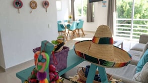 A room with a large window, a TV mounted on the wall, and a colorful woven hat on a stand. - Family Suite | 2BR, 2 Bath, Pool & 24h Security (Cancún)