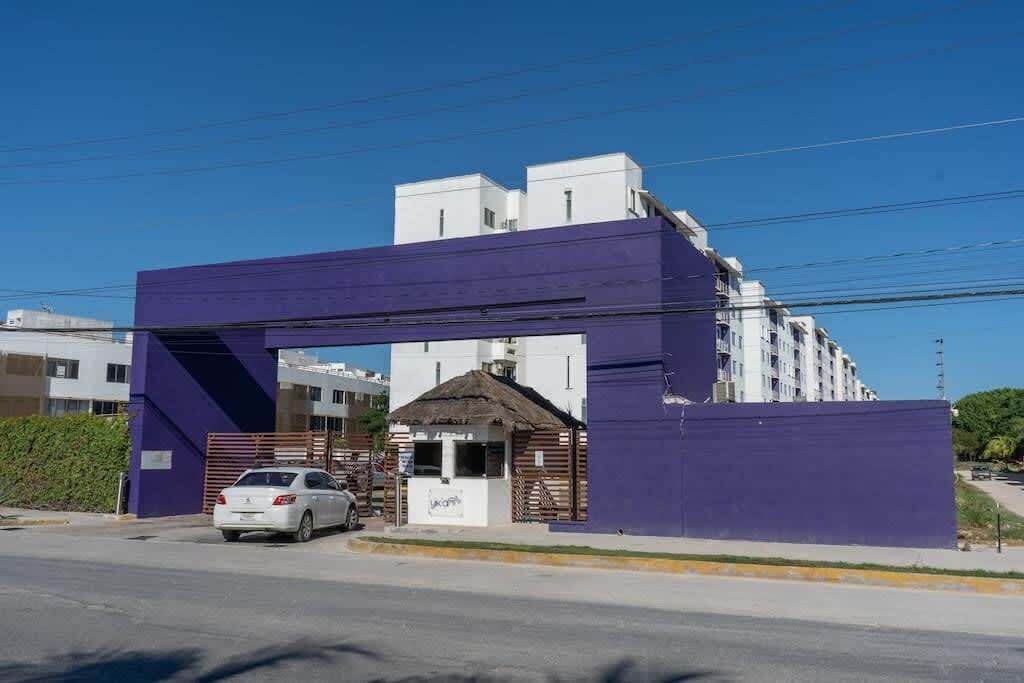 A building with a purple entrance, a white car parked in front, and a small structure with a thatched roof.