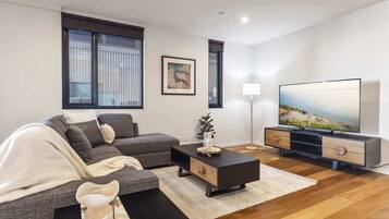 A modern living room with a sectional sofa, a coffee table, a flat-screen TV, and a floor lamp.