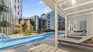 A modern building with a swimming pool, lounge chairs, and a covered seating area. - Refined 2-Bed With Luxurious Building Amenities (Belconnen)