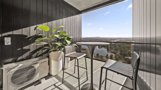 A balcony with a table and chairs, a potted plant, and a view of a landscape. - Refined 2-Bed With Luxurious Building Amenities (Belconnen)