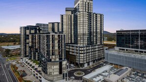 A modern high-rise building with multiple floors, large windows, and a prominent corner structure. - Refined 2-Bed With Luxurious Building Amenities (Belconnen)