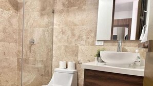 A modern bathroom with a glass shower enclosure, a white toilet, a wooden vanity with a large sink, and a mirror above the vanity. - Modern Studio · Rooftop Pool · Near 5th Ave (Playa del Carmen)