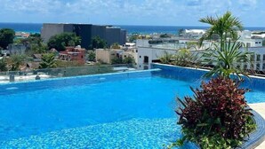 An infinity pool with a clear view of the ocean and buildings in the background. - Modern Studio · Rooftop Pool · Near 5th Ave (Playa del Carmen)