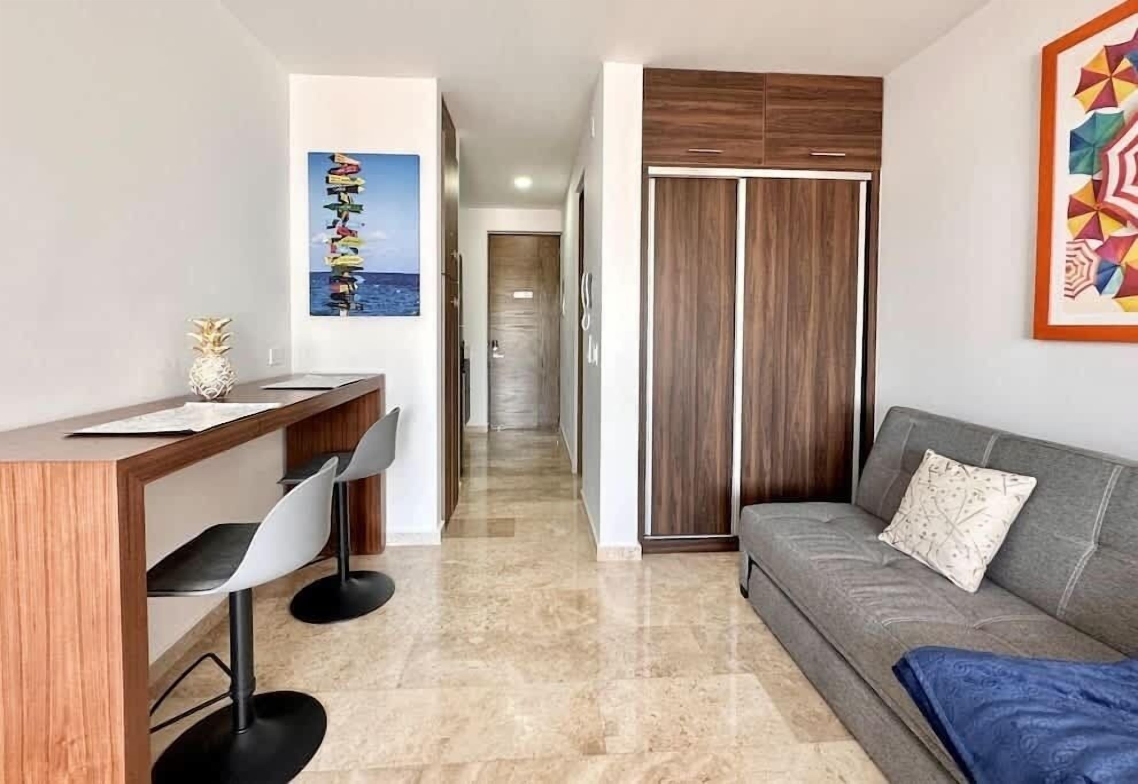 Un salon moderne avec un canapé, un coin repas comprenant une table et des chaises, un meuble en bois et un couloir menant à une autre pièce.