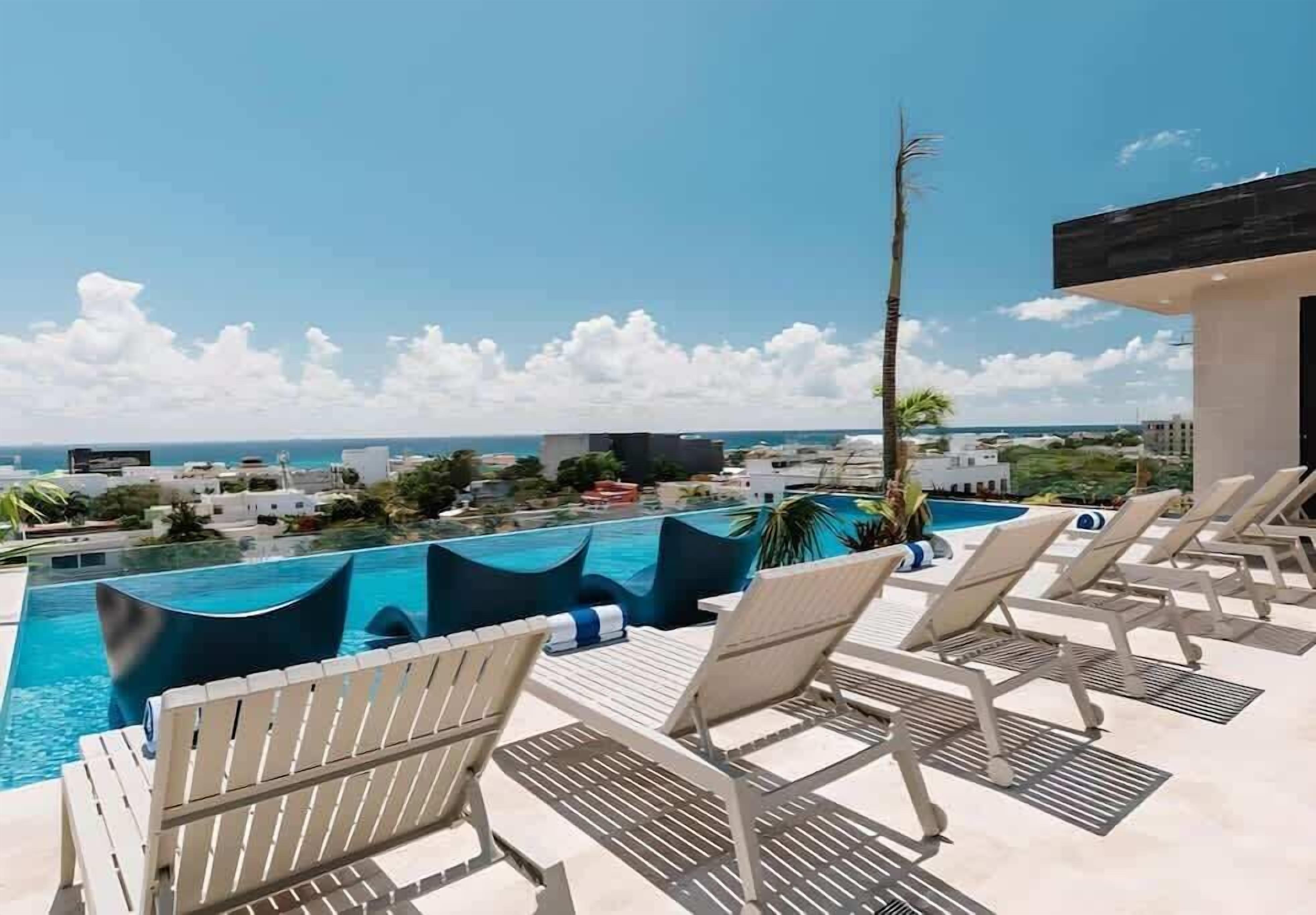 A rooftop pool area with lounge chairs and a view of the ocean.