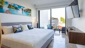 A modern hotel room with a large bed, a desk, a flat-screen TV, and a balcony with a view of the sea. - Modern Studio · Rooftop Pool · Near 5th Ave (Playa del Carmen)