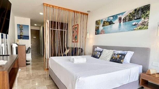 A modern hotel room with a large bed, a desk, and a painting of a coastal scene. - Modern Studio · Rooftop Pool · Near 5th Ave (Playa del Carmen)